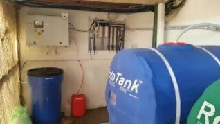 Wall-mounted Envirolyte generator and filtration assembly beside water storage tanks